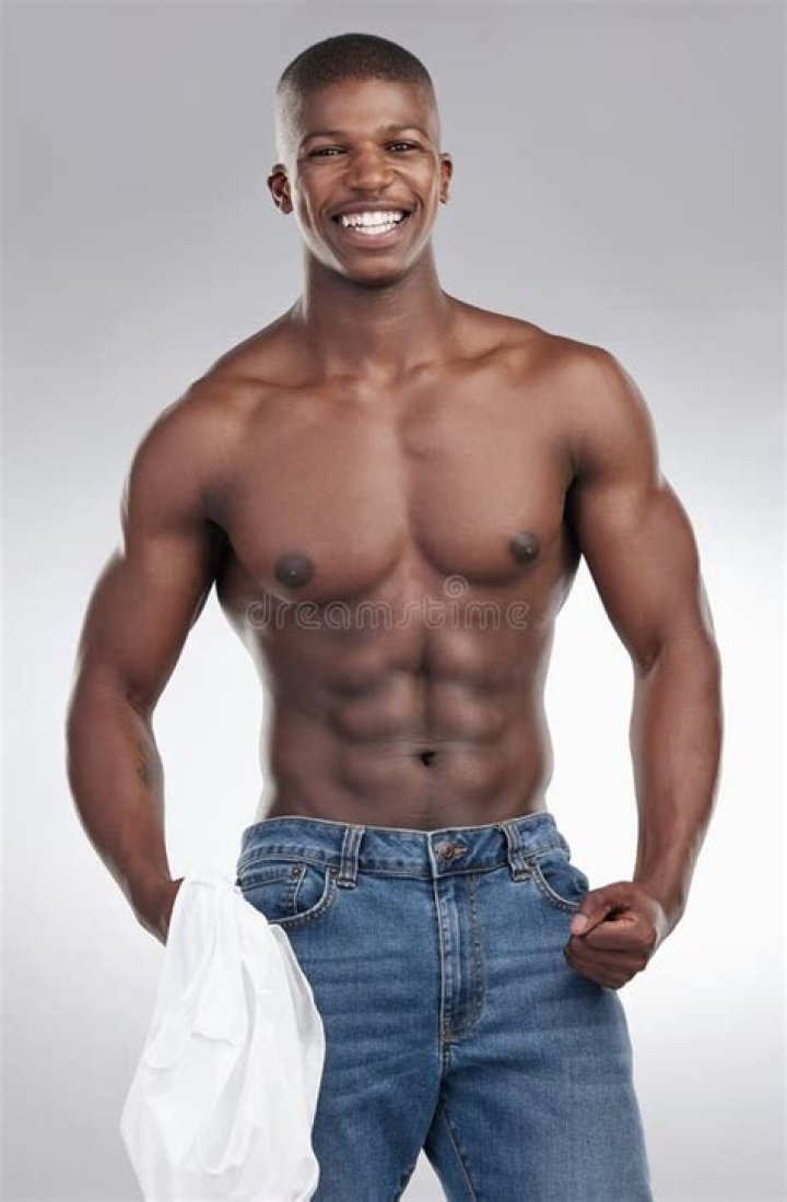 a man with no shirt standing in front of a curtain wearing white pants and a cross necklace